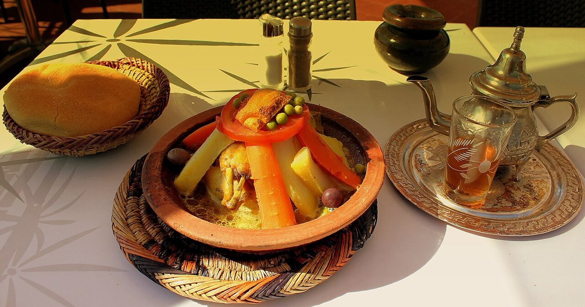 Tajín de pollo con verduras, pan, tetera y vaso de té con hierbabuena en una mesa de Marrakech